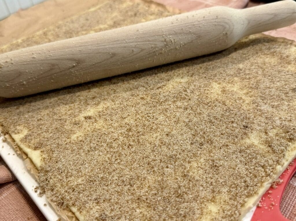 Using a rolling pin to lightly press the sugar onto the pastry